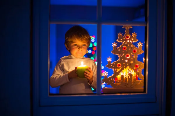 Liten unge pojke står vid fönstret i juletid och hålla — Stockfoto