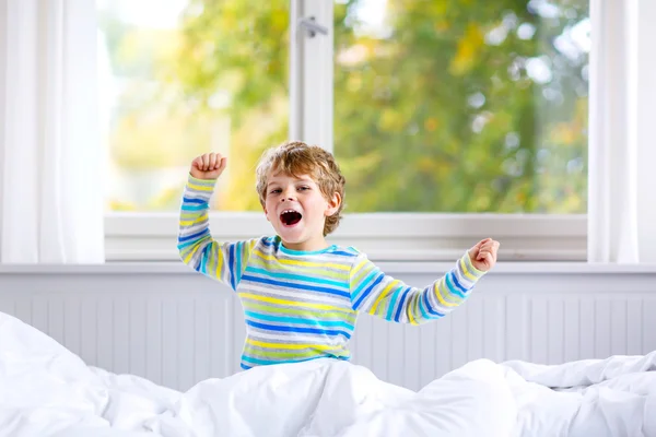 Adorable happy little kid boy after sleeping in his white bed in colorful pajama — Stock Photo, Image