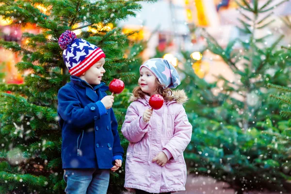 Двое маленьких детей едят кристаллизованное яблоко на Рождественской ярмарке — стоковое фото