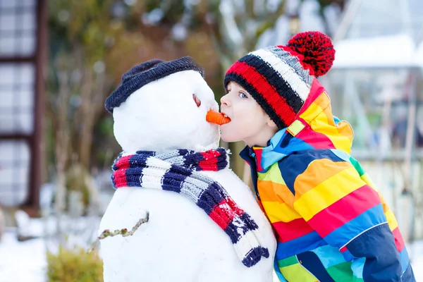 Niño gracioso en ropa colorida haciendo un muñeco de nieve, al aire libre — Foto de Stock