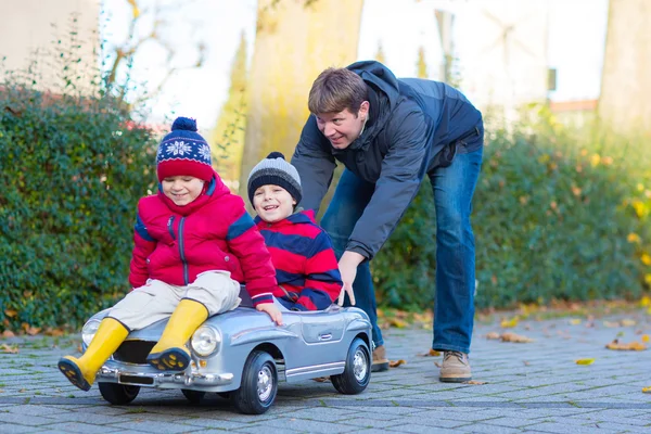 Dos niños pequeños niños y padre jugando con el coche, al aire libre — Foto de Stock