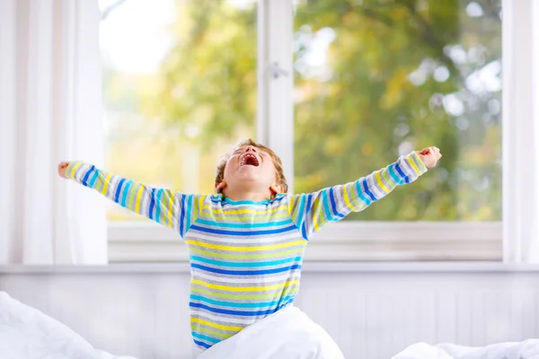 Menino pequeno feliz depois de dormir na cama em roupas de noite coloridas — Fotografia de Stock