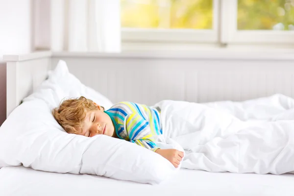 Pequeno garoto despreocupado dormindo na cama em roupas de noite coloridas . — Fotografia de Stock