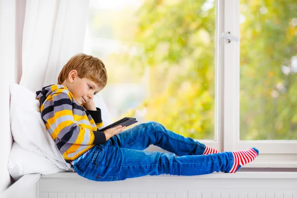 Маленький школьник читает книгу или электронную книгу за окном — стоковое фото
