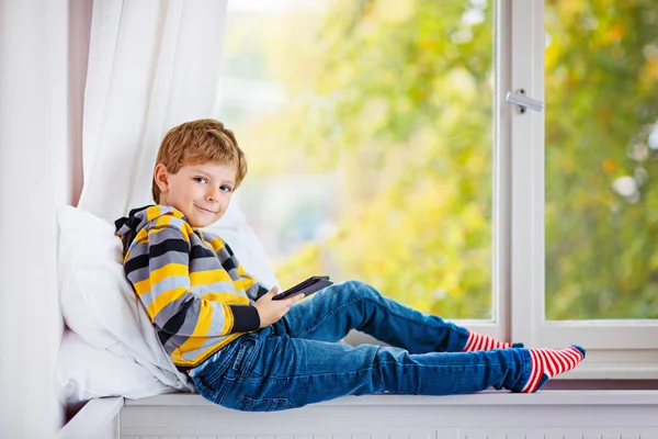 Malý chlapec škole číst knihu nebo ebook do okna — Stock fotografie
