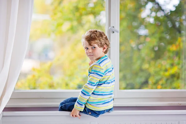 Little kid boy seduto vicino alla finestra e guardando gli alberi autunnali — Foto Stock
