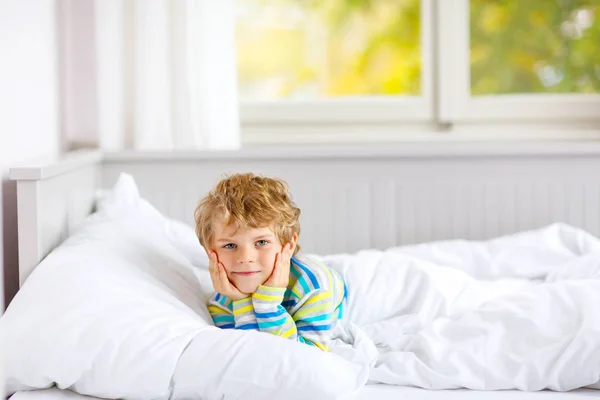 Menino pequeno feliz depois de dormir na cama em roupas de noite coloridas — Fotografia de Stock