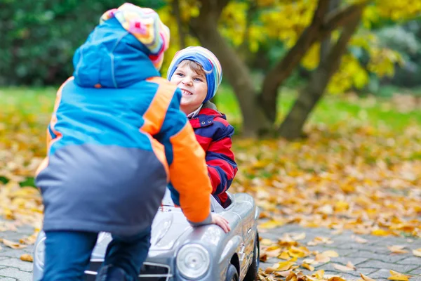 Fratello che spinge l'auto per il bambino. Felicità, divertimento, svago nel parco autunnale . — Foto Stock