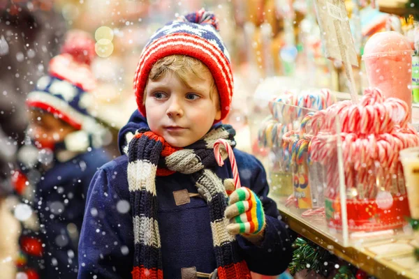 Little kid boy with candy cane stand on Christmas market — Stock Photo, Image