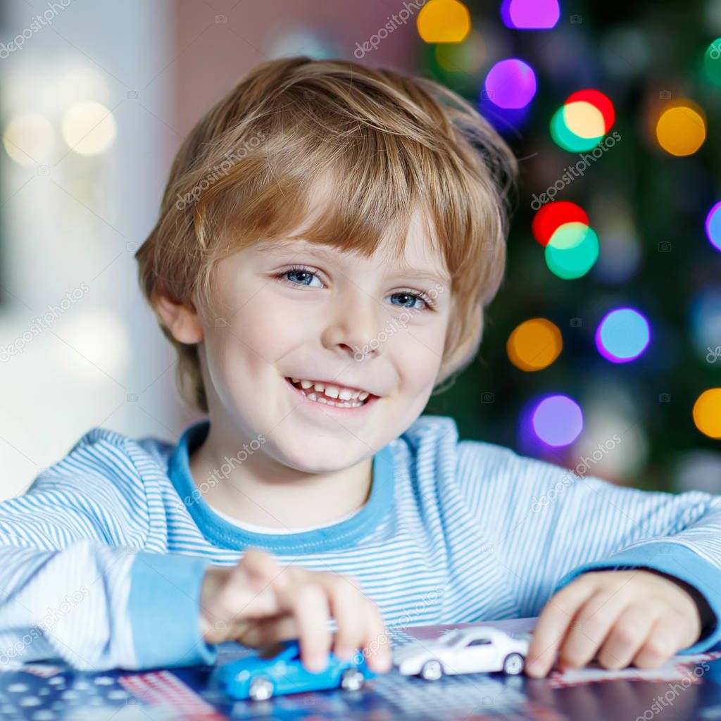 Ragazzo bello bambino che gioca con auto e giocattoli a casa al coperto bambino divertente divertirsi con i regali Luci colorate di Natale sul fondo