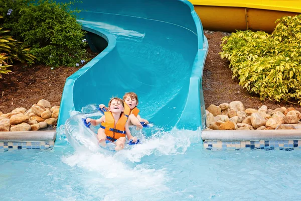 Bambini entusiasti nel parco acquatico cavalcando sullo scivolo con galleggiante — Foto Stock