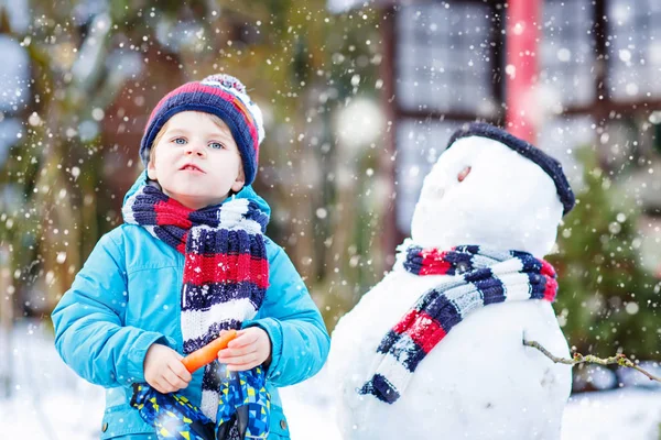 Funny kid boy i färgglada kläder att göra en snögubbe, utomhus — Stockfoto