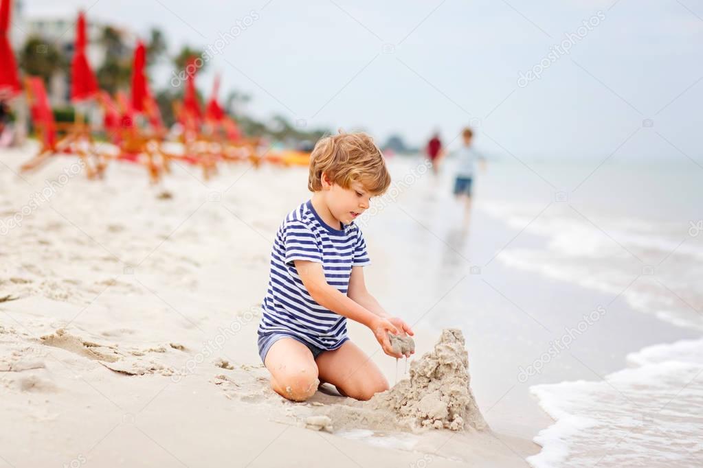 Little kid boy having fun with building sand castles