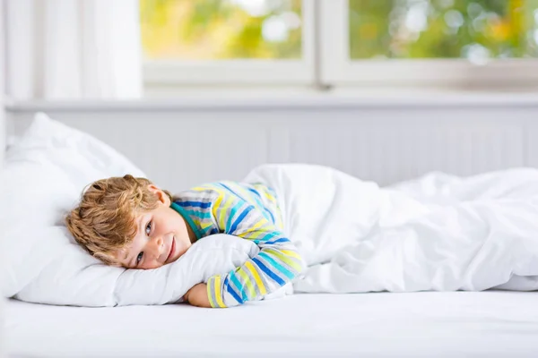Счастливый маленький мальчик после сна в кровати в красочной ночной рубашке — стоковое фото