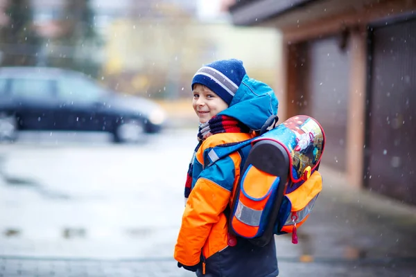 Χαρούμενο παιδί που διασκεδάζει με το χιόνι στο δρόμο για το σχολείο. — Φωτογραφία Αρχείου