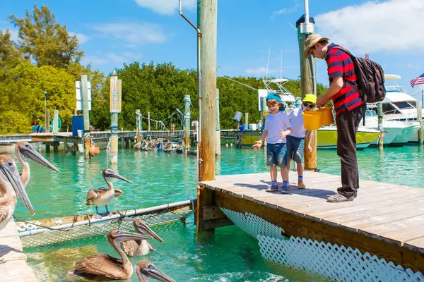 Padre y dos niños alimentando peces y pelícanos —  Fotos de Stock