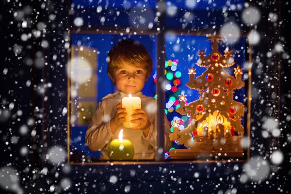 Kleiner Junge steht zur Weihnachtszeit am Fenster und hält — Stockfoto