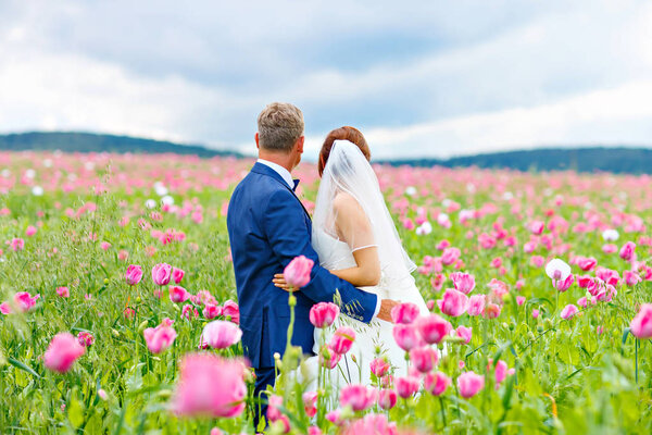 Happy wedding couple in pink poppy field