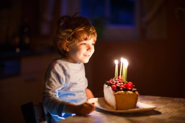 Little kid boy celebrating his birthday and blowing candles on cake clipart