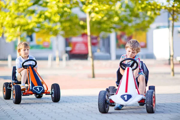 Two little kid boys driving pedal race car in summer garden — Stock Photo, Image