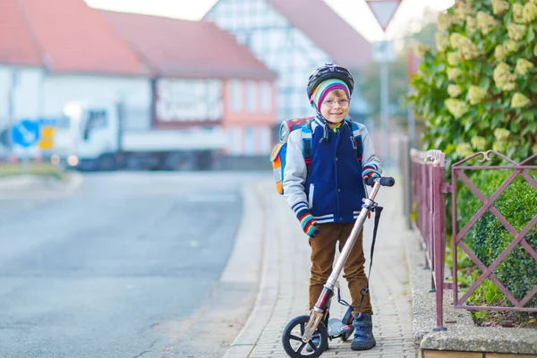 Petit garçon en casque chevauchant avec son scooter dans la ville — Photo