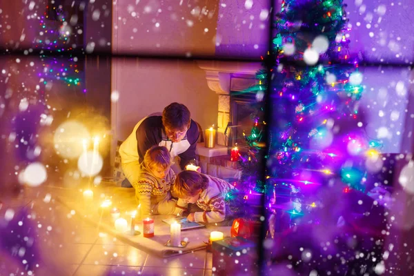 Joven padre y sus pequeños hijos sentados junto a una chimenea en C —  Fotos de Stock