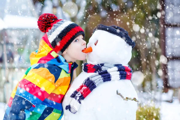 Garoto engraçado em roupas coloridas fazendo um boneco de neve, ao ar livre — Fotografia de Stock