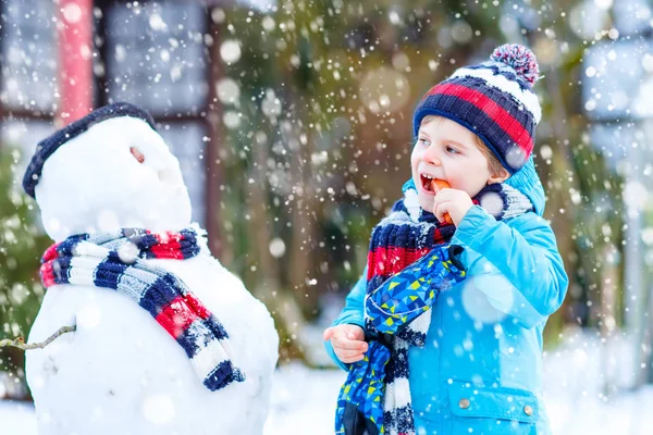 Enfant drôle garçon en vêtements colorés faire un bonhomme de neige, en plein air — Photo
