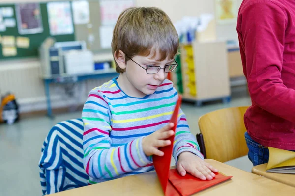 Ragazzo della scuola con gli occhiali giocare con carta colorata e fare figure geometriche — Foto Stock