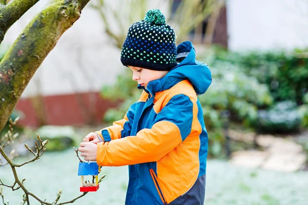 小家伙挂鸟房子在冬天喂养的树上的男孩 — 图库照片