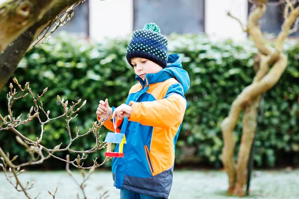 Маленький мальчик висит птичий домик на дереве для кормления зимой — стоковое фото