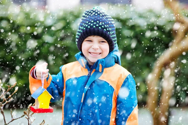 Kleine jongen jongen opknoping vogelhuisje op boom voor het voederen in de winter — Stockfoto