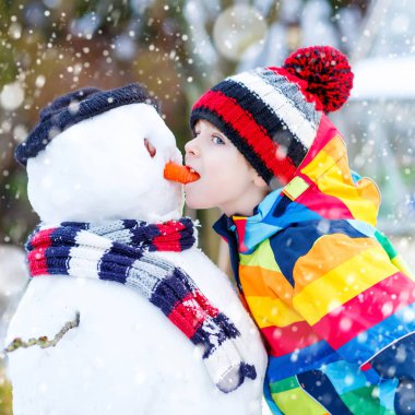 Komik çocuk çocuk renkli giysiler açık havada bir kardan adam yapma