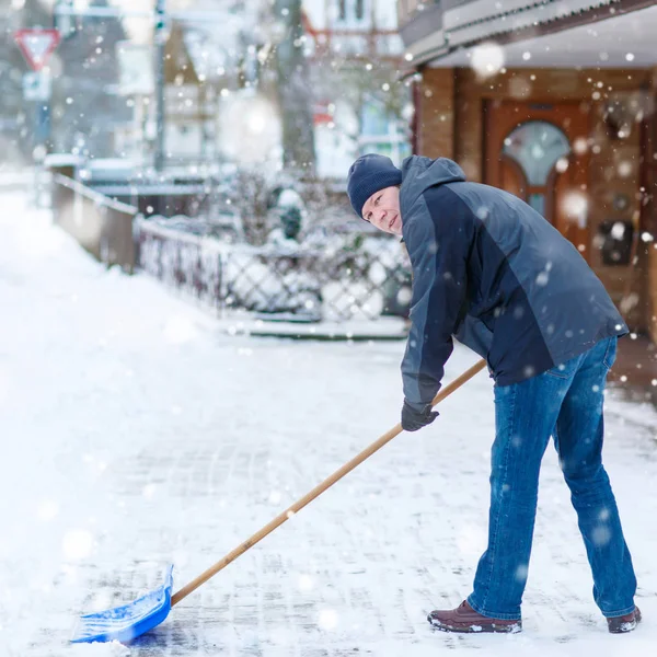 Чоловік зі сніжною лопатою чистить тротуари взимку — стокове фото
