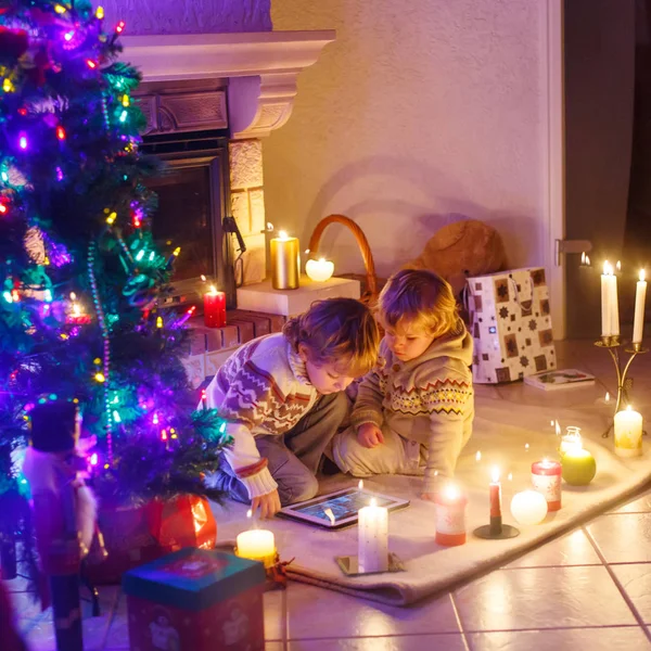 Två små barn sitter vid en öppen spis hemma på jul — Stockfoto