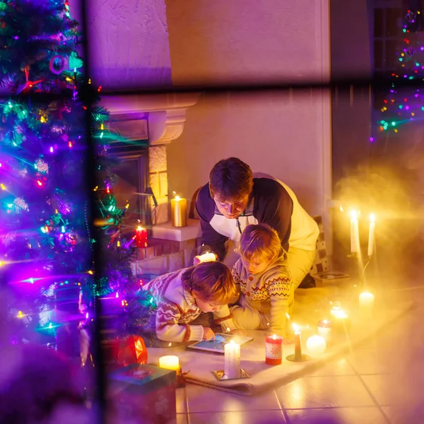 Junger Vater und seine kleinen Kinder sitzen am offenen Kamin auf dem — Stockfoto