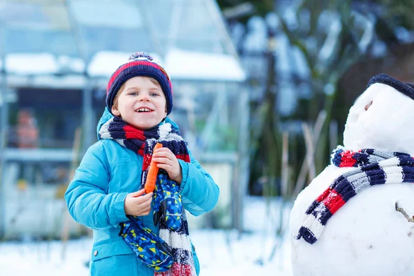 Funny kid boy making a snowman in winter outdoors — Stock Photo, Image