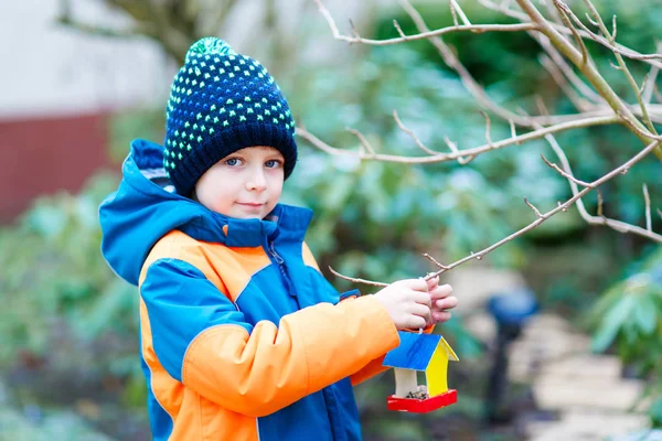 Petit garçon accroché maison d'oiseau sur l'arbre pour se nourrir en hiver — Photo