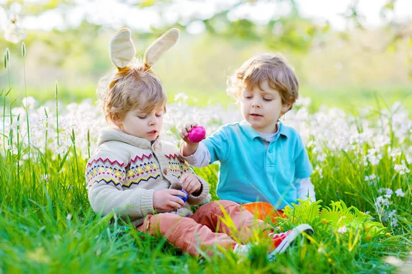 Zwei kleine Freunde in Osterhasenohren bei der Eiersuche — Stockfoto