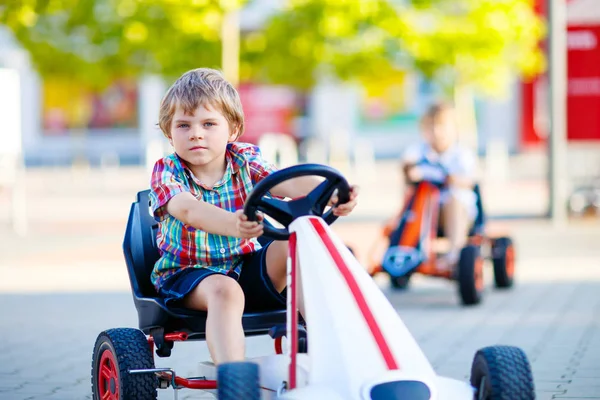 Два активных маленьких мальчика за рулем педали гоночного автомобиля летом — стоковое фото