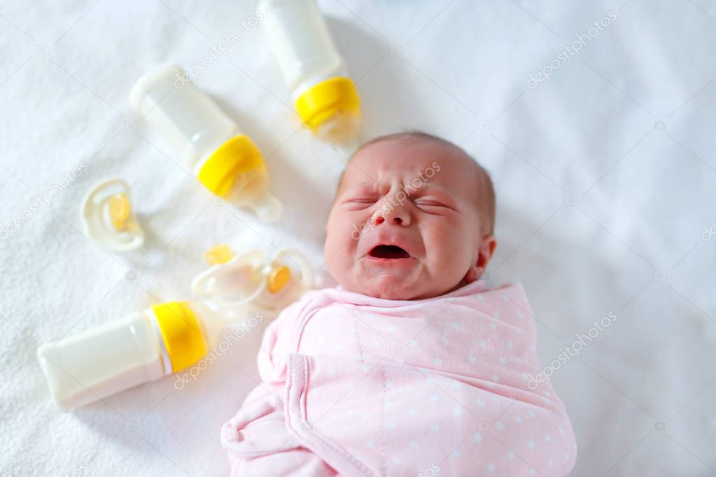 Crying newborn baby girl with nursing bottles. Bottle feeding