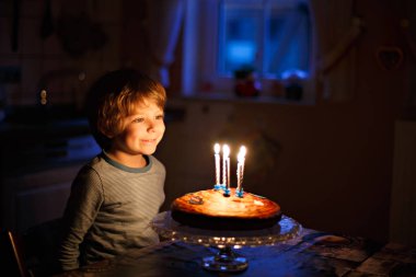 Little kid boy celebrating his birthday and blowing candles on cake clipart