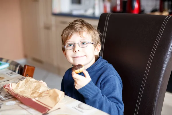 Kleine school jongen eten donut binnen in een kantine. — Stockfoto