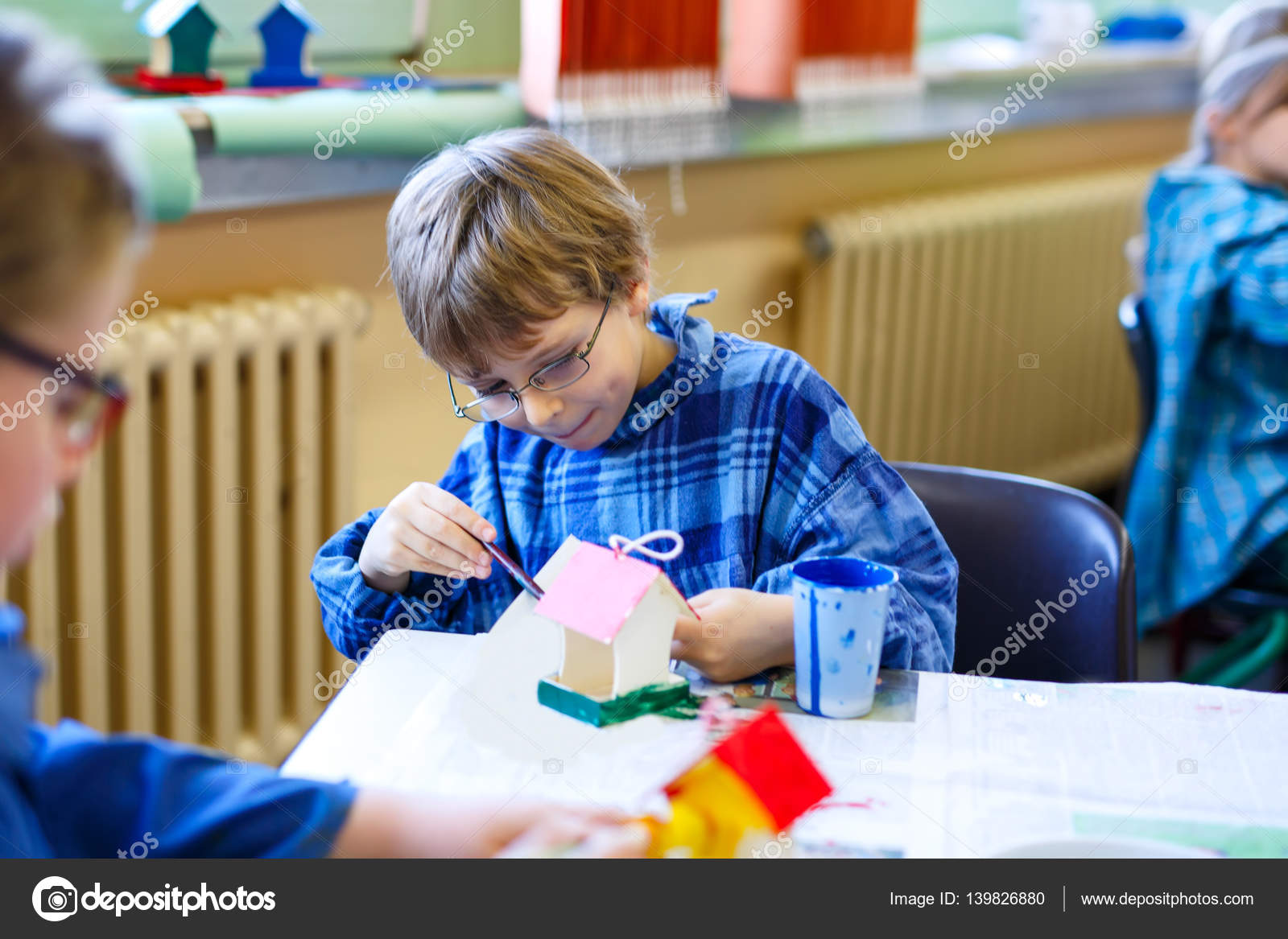 Piccolo ragazzo del bambino scuola con occhiali colorare la casa di uccello con gli acquerelli —