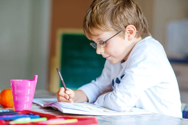 Niño de la escuela feliz con gafas en casa haciendo tarea —  Fotos de Stock