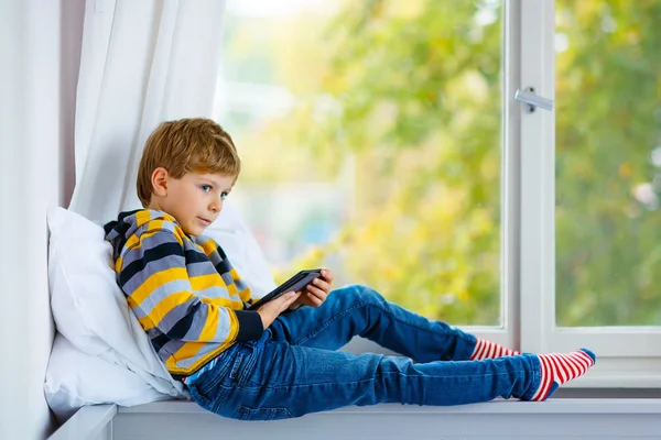 Маленький школьник читает книгу или электронную книгу за окном — стоковое фото