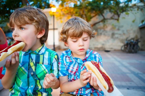 Dwa małe dziecko chłopców jedzenie hot dogi na zewnątrz — Zdjęcie stockowe