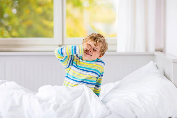 Glad liten unge pojke efter att ha sovit i sängen i färgglada nattkläder — Stockfoto