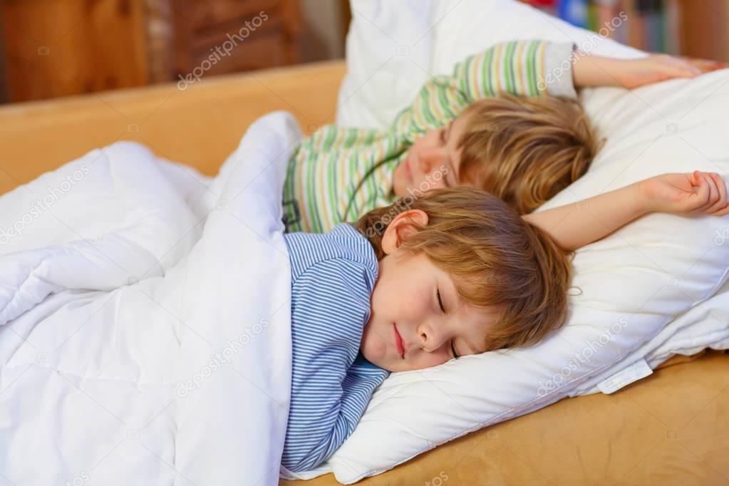 Two little blond sibling boys sleeping in bed