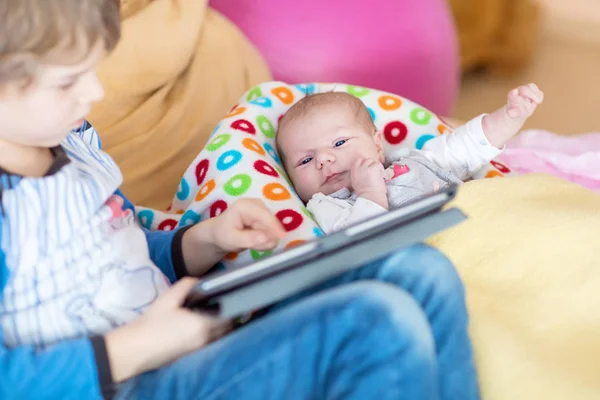 Preschool kid boy playing games tablet computer. Cute newborn baby looking on brother. — Stock Photo, Image